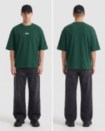 Men's green oversized t-shirt with small logo, paired with black jeans and cap.